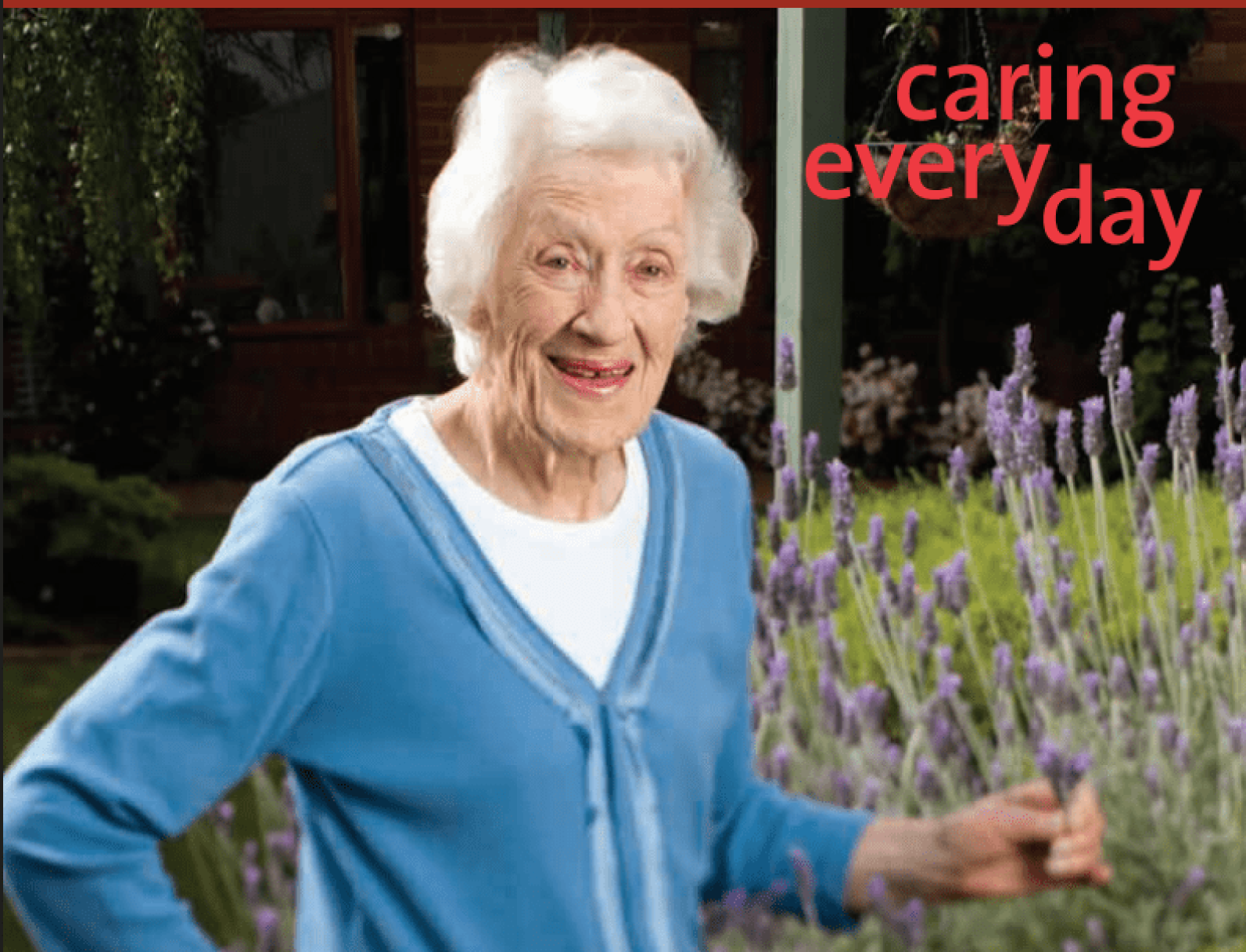 An older adult standing beside a flowering lavender garden, wearing a light blue cardigan over a white top. The image is set in a landscaped outdoor courtyard with greenery and purple flowers in bloom. Red text in the top-right corner reads: “caring everyday”.