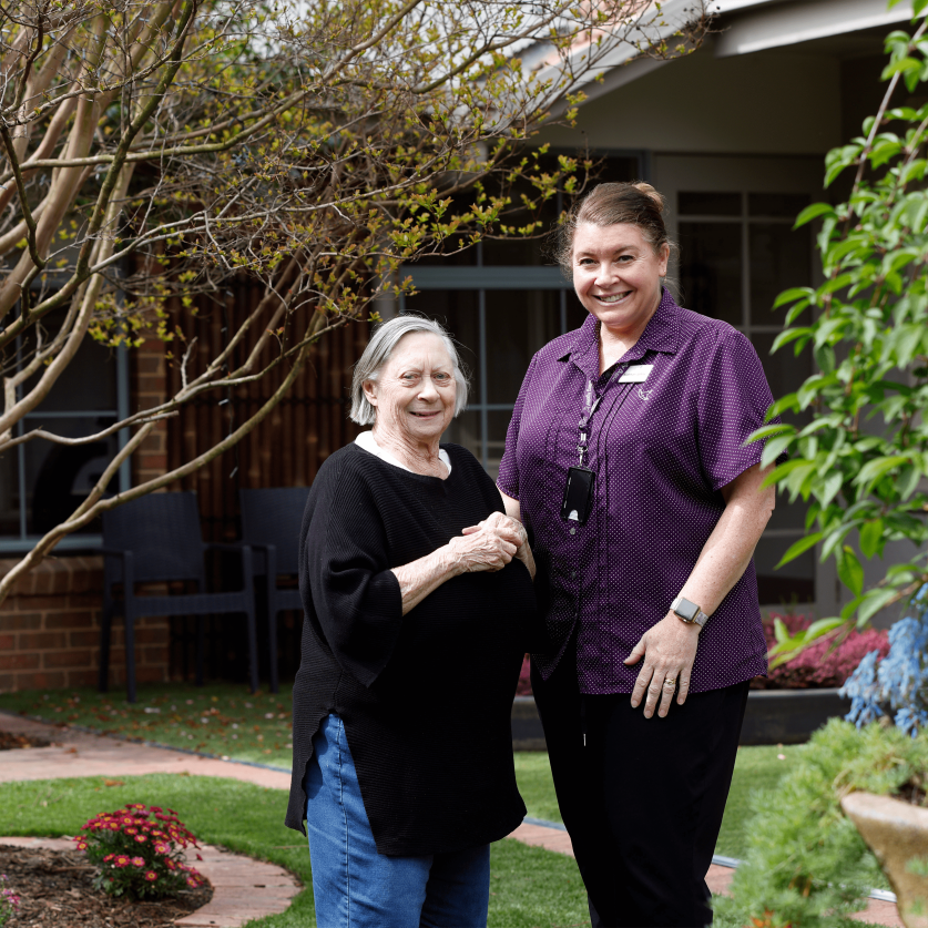 Staff member standing beside resident in garden smiling.