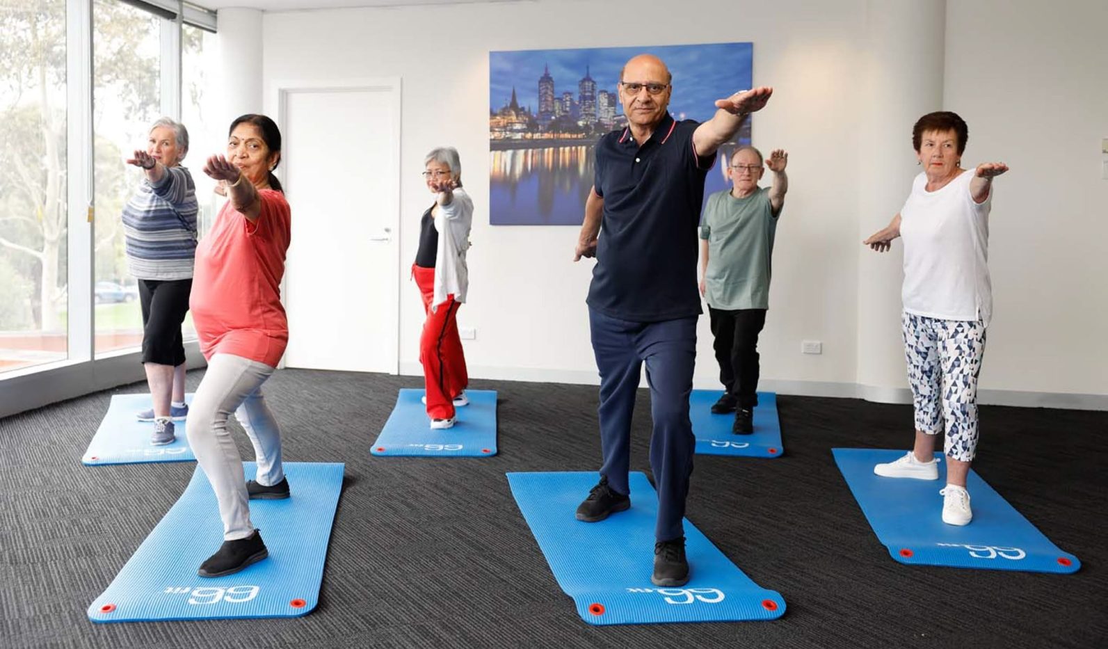 A group of Uniting AgeWell customers are pictured in a fitness class, with each standing on a yoga mat.