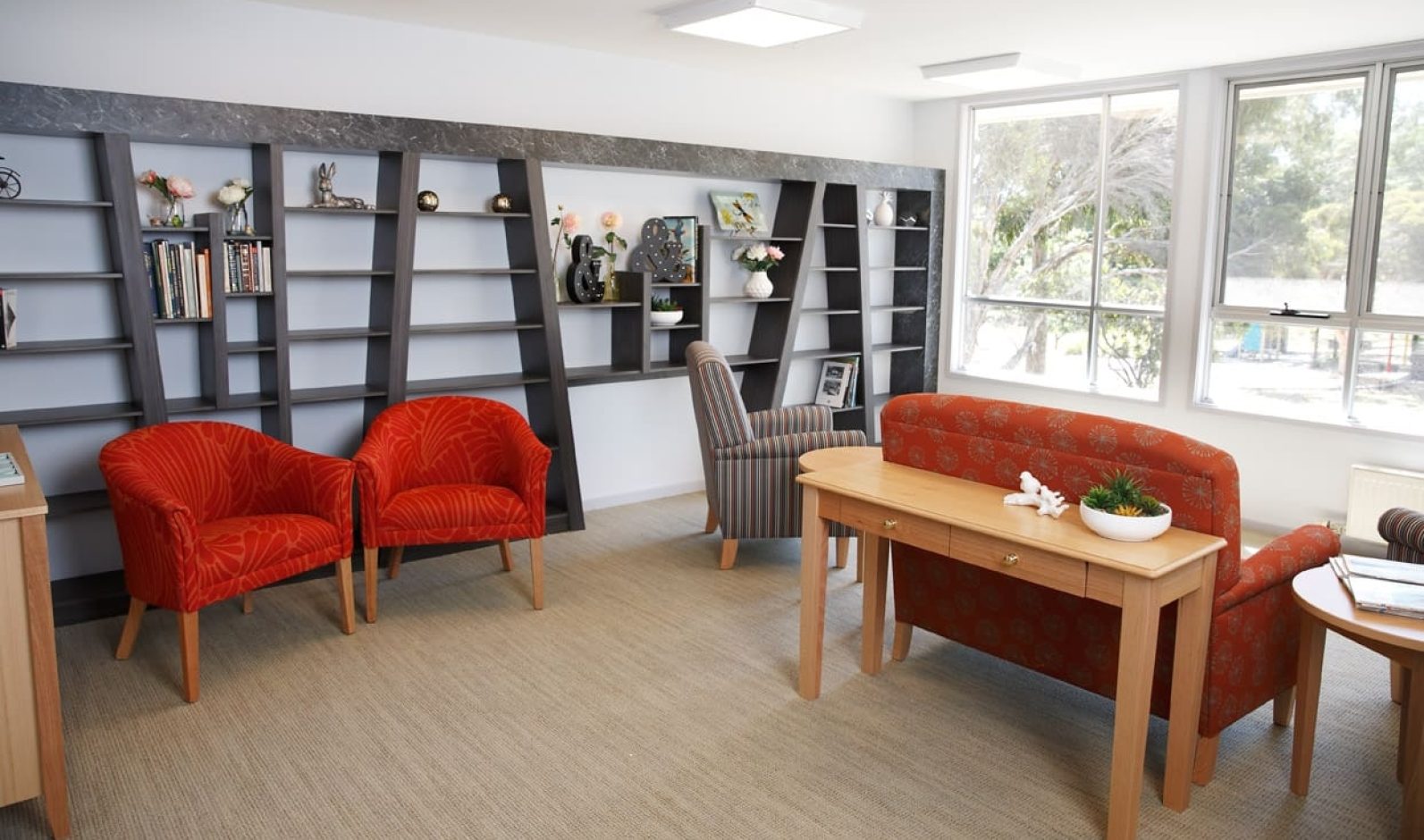 A comfortable and spacious lounge room is featured, there are chairs and a shelf to be filled by books.