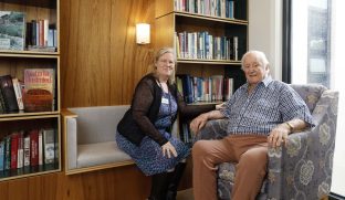 A staff member and a resident are pictured sitting in the room with wood elements