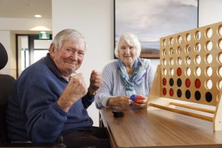 Two residents are looking at the camera while playing connect four