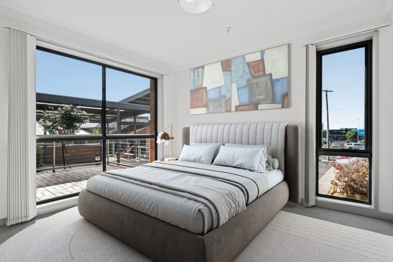 The bedroom is captured with a bed in the middle and windows on two sides of the room.