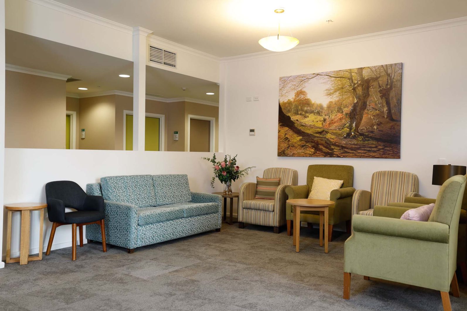 There are seating areas, including a blue couch and a green couch in the lounge. There are a coffee tables in the area and a painting of a garden is on the wall.