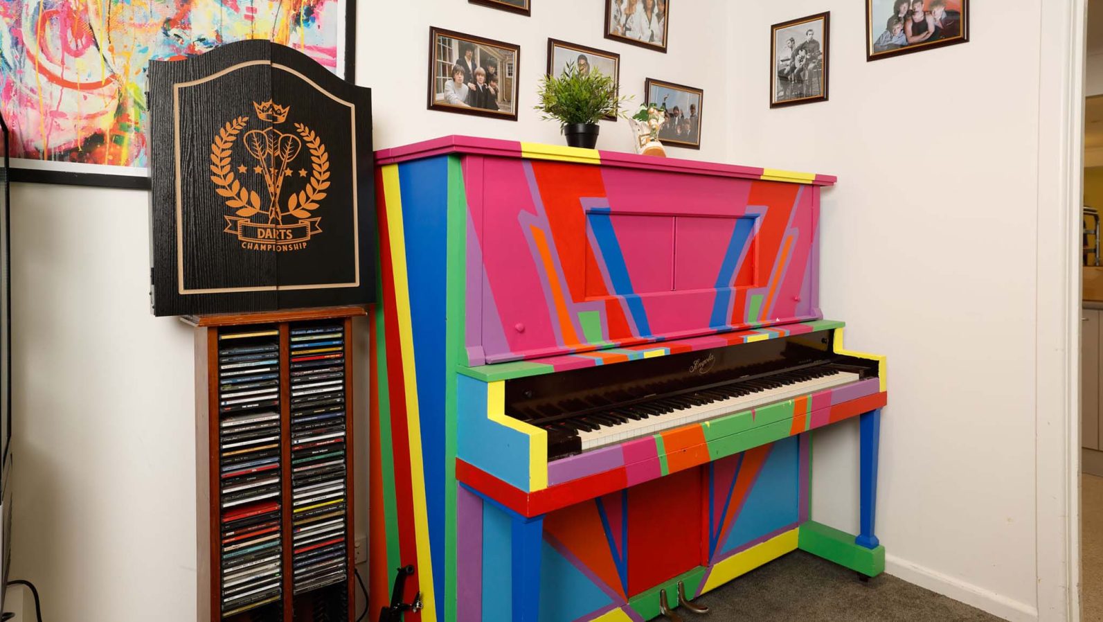 A piano painted in rainbow colour is at the corner of the room with picture frames on the wall.