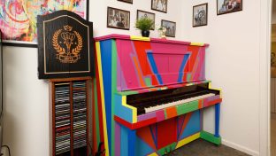 A piano painted in rainbow colour is at the corner of the room with picture frames on the wall.