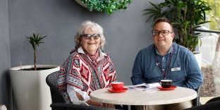 Chaplain and resident sitting at outdoor table for tea and coffee.