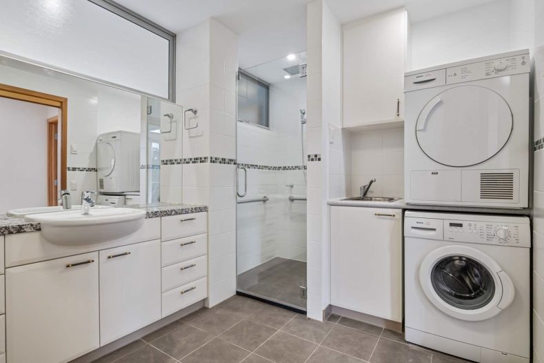 The bathroom area at Queenborough Rise is photographed. There is a washing machine and drying machine on the left side.