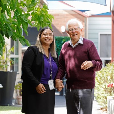 A resident and a staff member are pictured holding hands in the gardens of Kalkee Community Murray