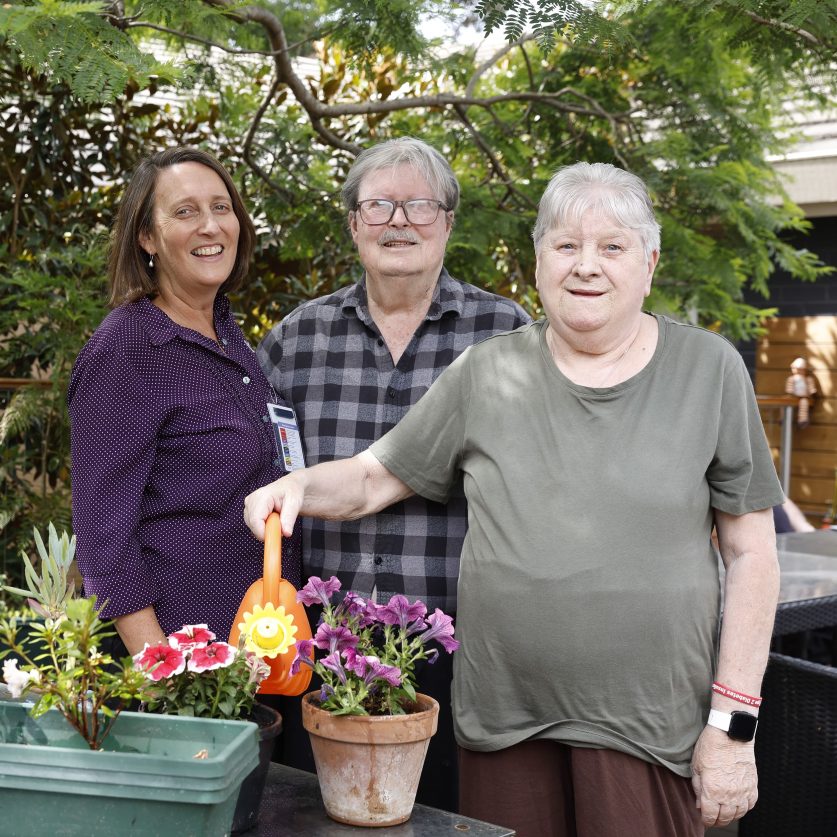 Two residents and a staff in the garden, with one resident watering flowers.
