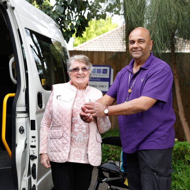A Uniting AgeWell staff member is holding a customer's hand next to a Uniting AgeWell van
