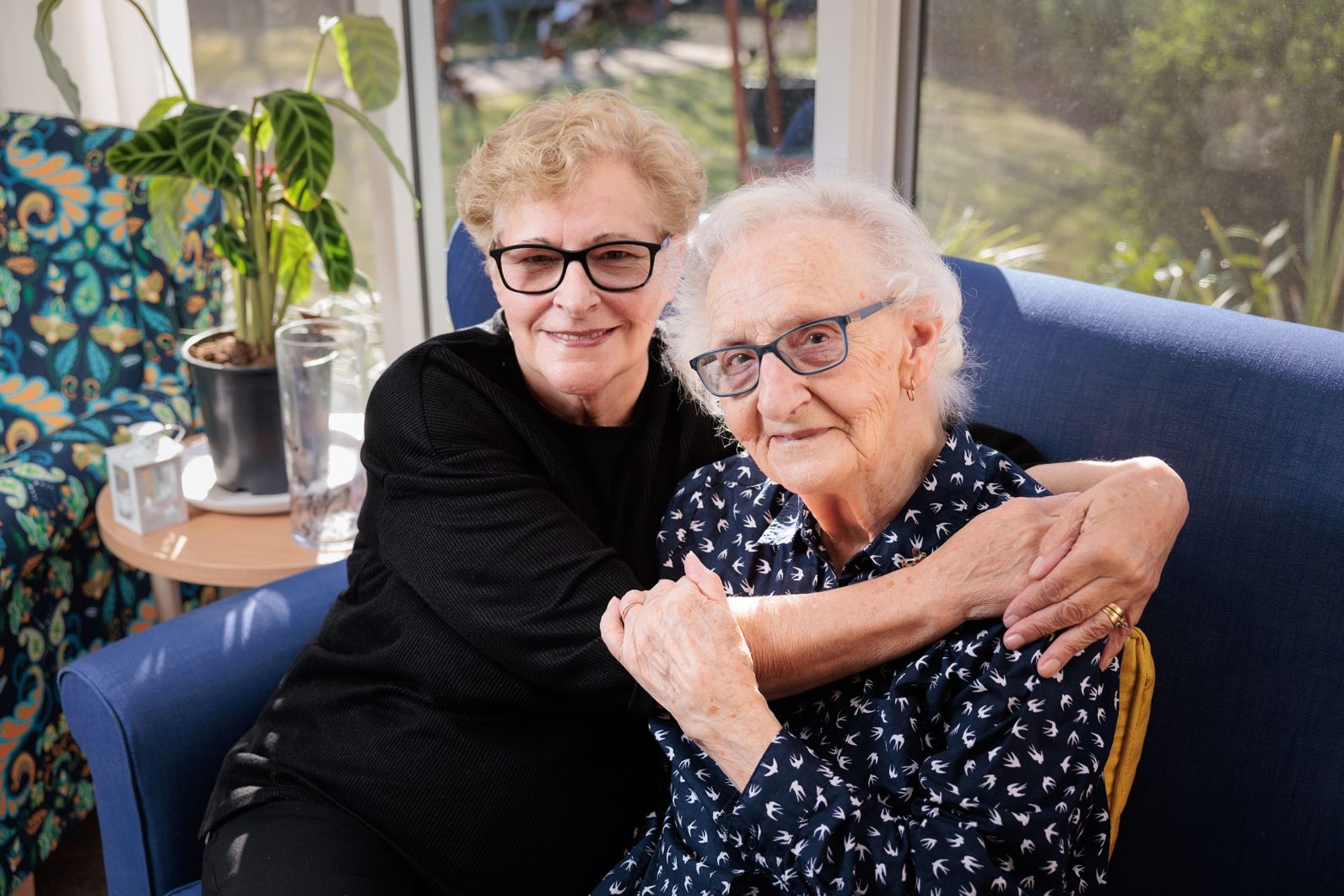 Two residents are hugging each other, smiling at the camera