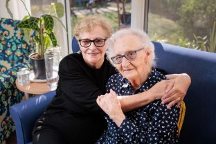 Two residents are hugging each other, smiling at the camera