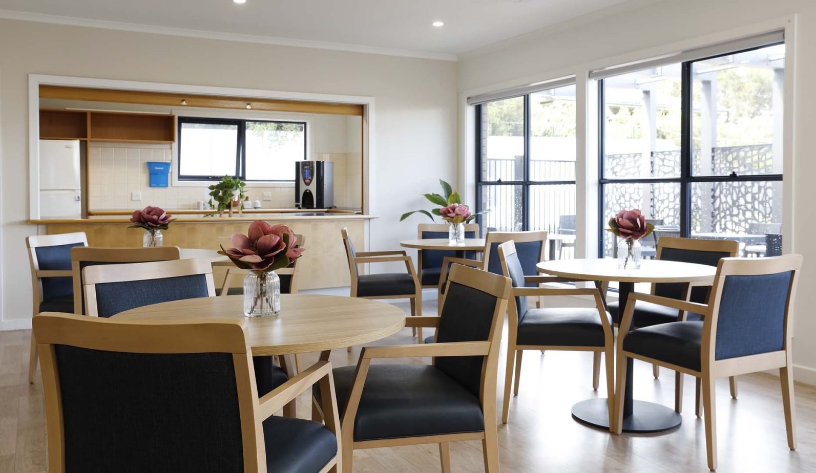 Dining chairs and tables in the foreground with a small kitchen pictured in the background