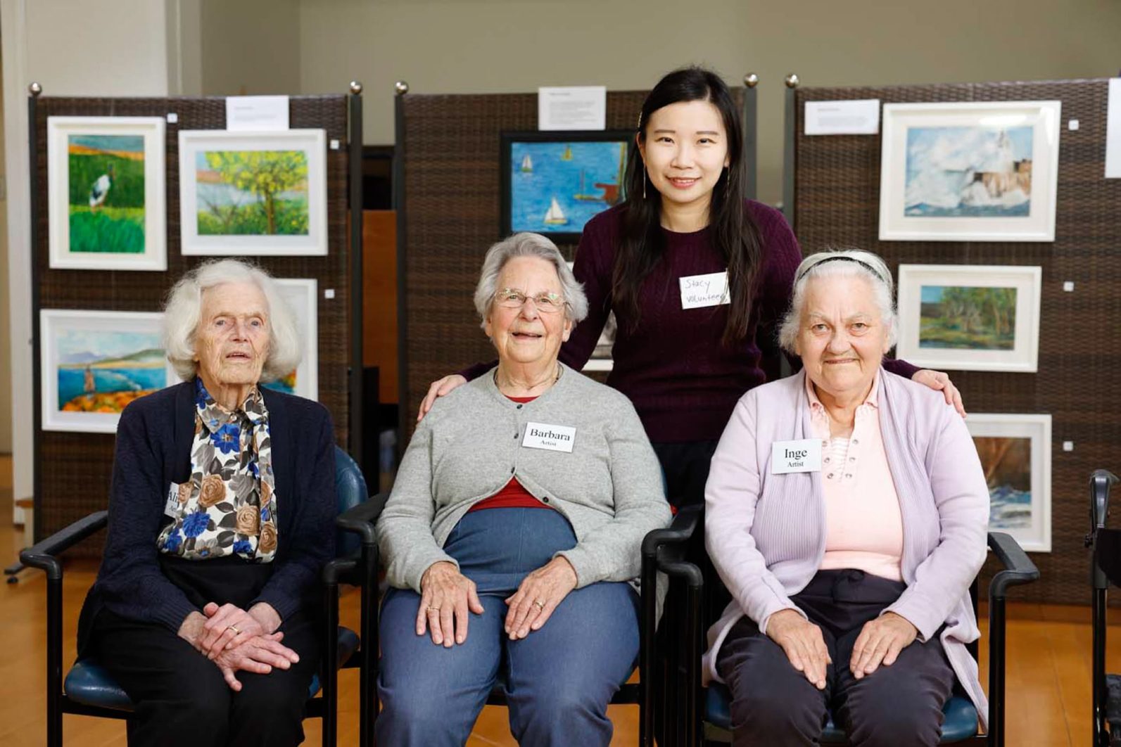 Four people are smiling at the camera, customers' artworks are featured behind them.