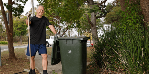 Person with rake next to green garbage bin.