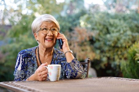 Person sitting at table in garden on their mobile phone with mug of tea,