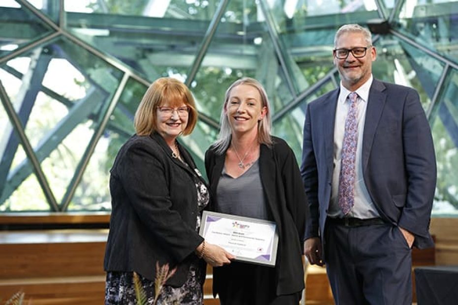 Three people on stage with certificate.