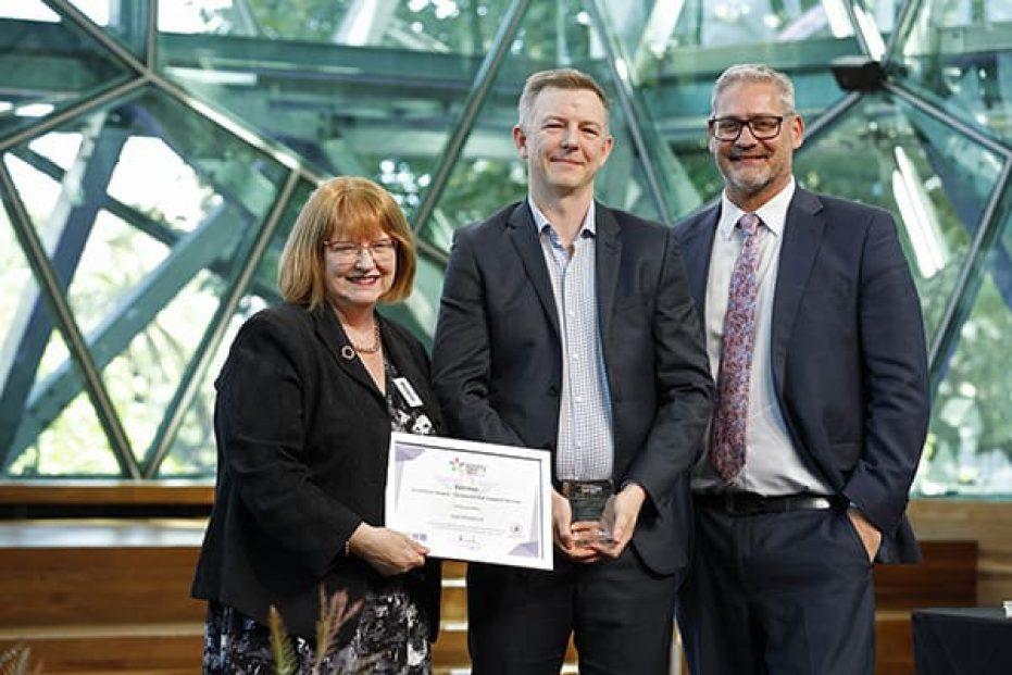 Three people on stage with certificate.