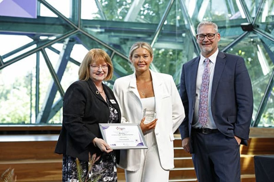 Three people on stage with certificate.