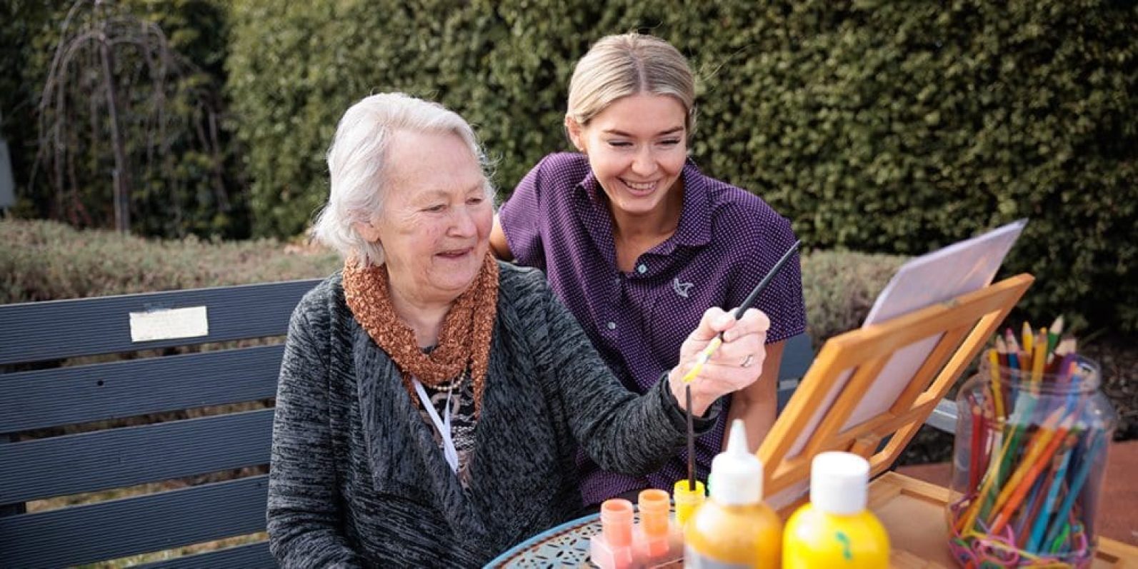 A staff member and a resident are painting in a garden