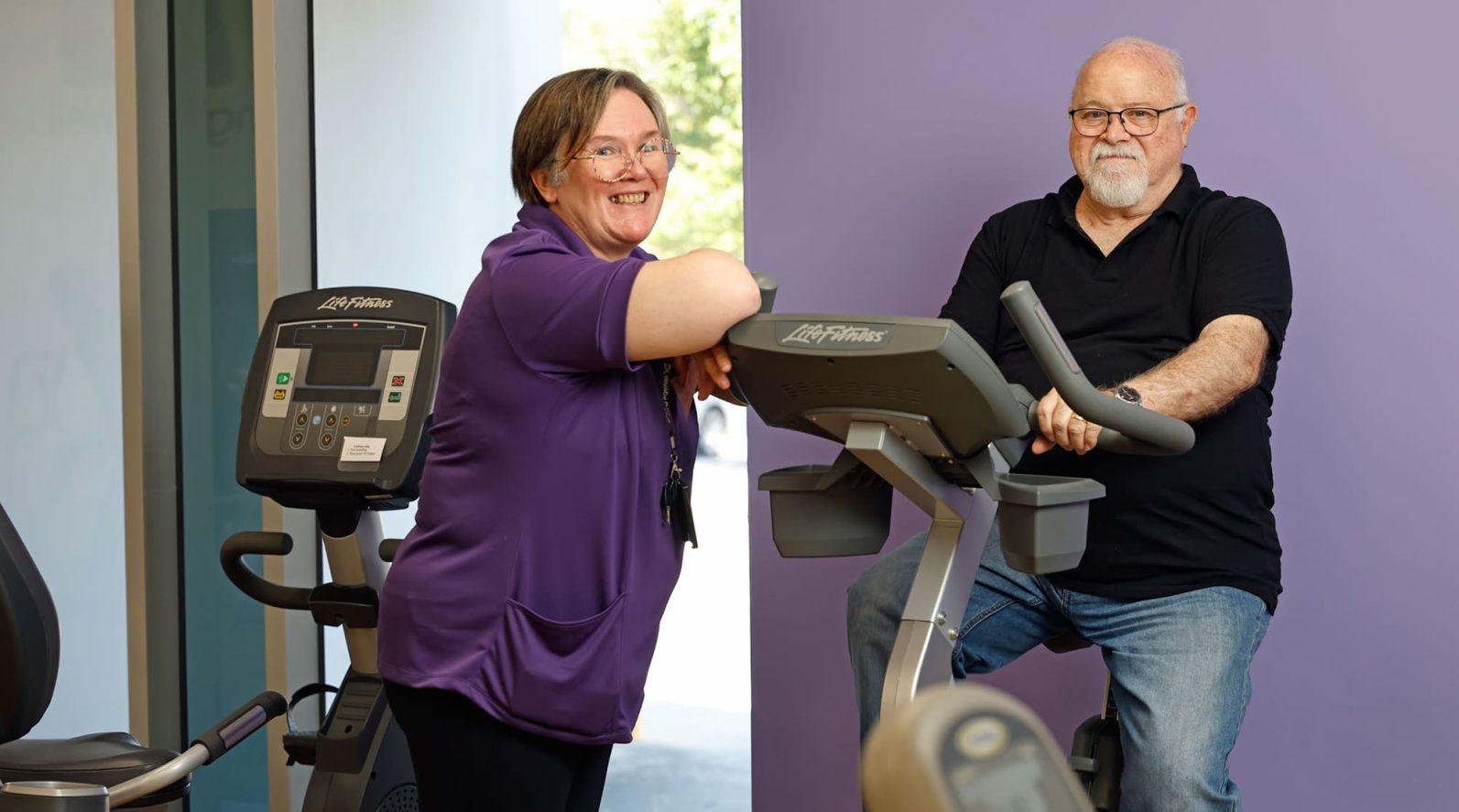Staff member standing beside customer on exercise bike.