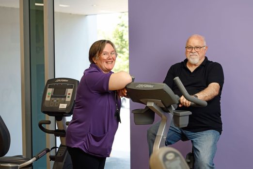 Staff member standing beside customer on exercise bike.