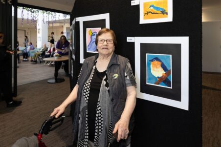 Resident standing in front of their painting at the Preston Art Exhibition
