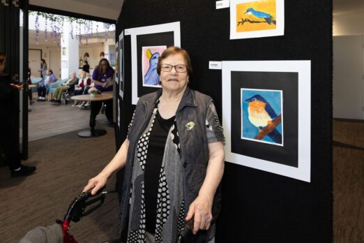 Resident standing in front of their painting at the Preston Art Exhibition