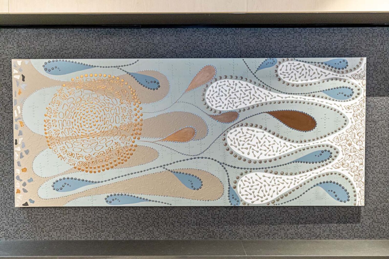 Abstract decorative wall artwork featuring flowing organic shapes in soft blue, beige, white and brown tones. Raised textured patterns, dotted lines and circular motifs create a nature-inspired design mounted on a dark textured wall.
