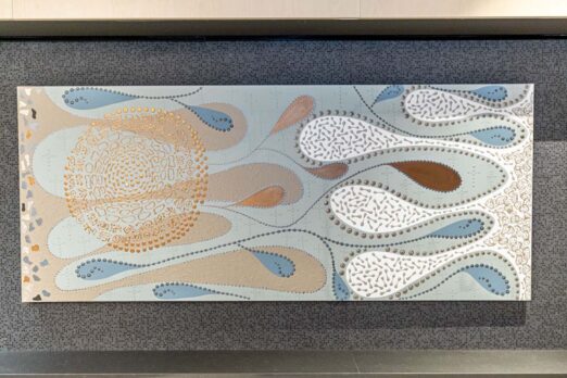 Abstract decorative wall artwork featuring flowing organic shapes in soft blue, beige, white and brown tones. Raised textured patterns, dotted lines and circular motifs create a nature-inspired design mounted on a dark textured wall.