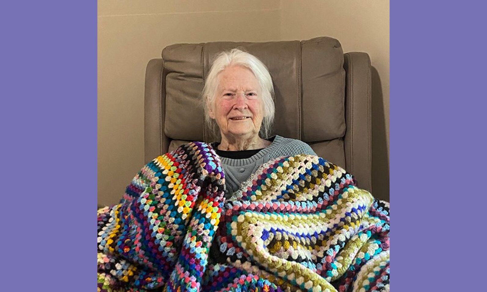 Janette Cunningham is photographed covered in colourful crocheted blankets in her room