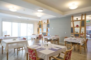 The image captures the dining area at Manor Lakes Community, featuring tables with four chairs at each of them.