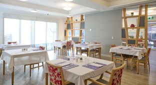 The image captures the dining area at Manor Lakes Community, featuring tables with four chairs at each of them.